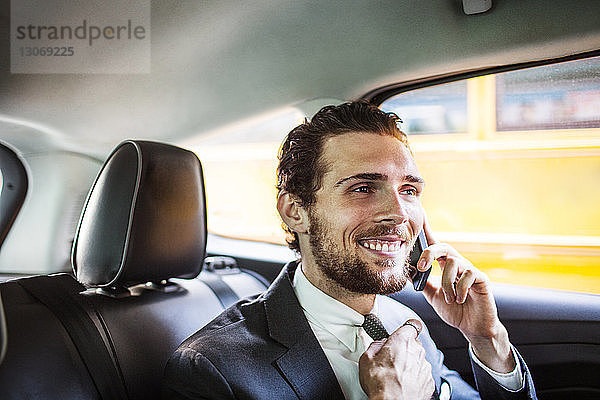 Lächelnder Geschäftsmann telefoniert während der Fahrt im Auto