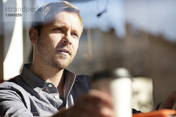 Mann mit Kaffeetasse schaut weg  während er im Café sitzt  durch Glas gesehen