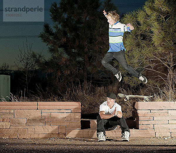 Mann mit Skateboard springt nachts über Freund