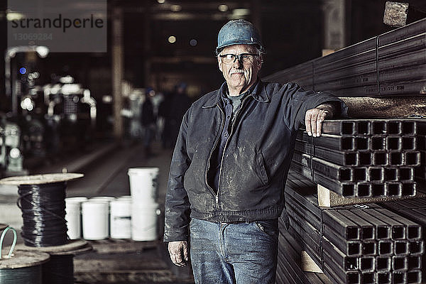 Porträt eines Mannes  der in der Fabrik an Metallrohren steht