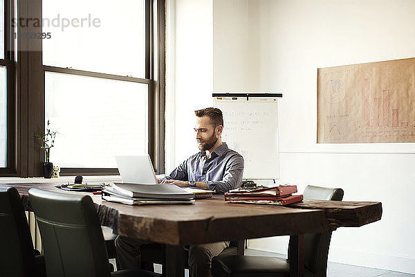 Geschäftsmann  der am Laptop arbeitet  während er im Büro am Schreibtisch sitzt