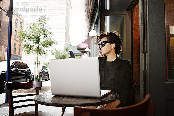 Frau mit Laptop-Computer sitzt im Straßencafé