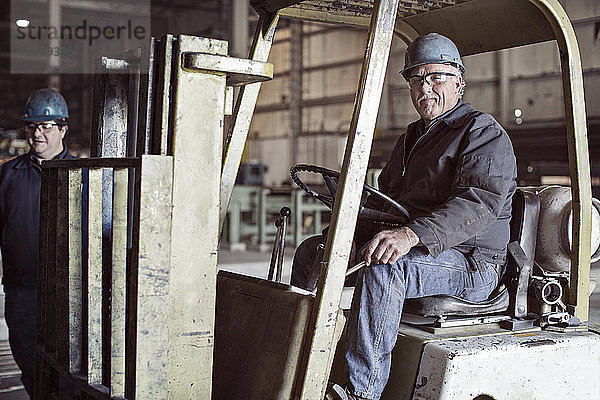 Porträt eines Mannes  der auf einem Gabelstapler in der Fabrik sitzt