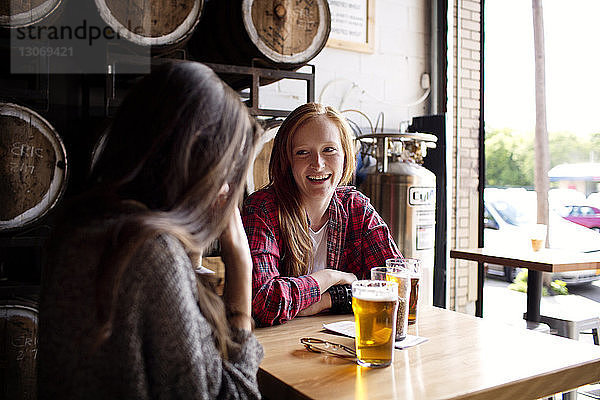 Fröhliche Freunde unterhalten sich bei einem Bier am Tisch in einer Brauerei