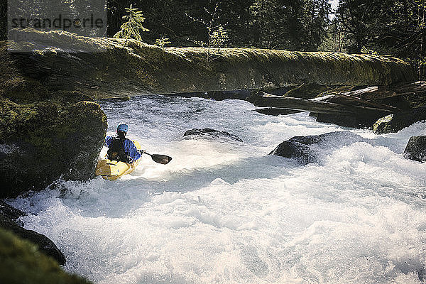 Mann mit Kajak im Fluss unter umgestürztem Baumstamm