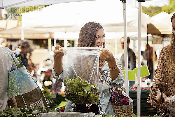 Lächelnde Frau mit Freundin beim Gemüseeinkauf am Marktstand