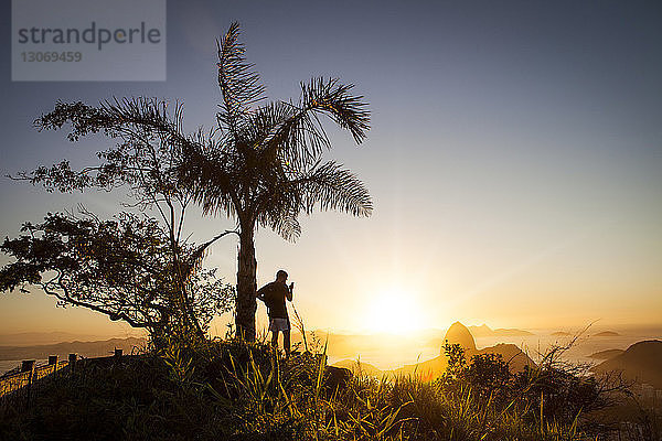 Mann benutzt Mobiltelefon  während er bei Sonnenuntergang am Zuckerhut steht