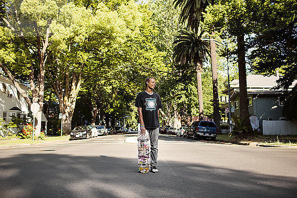 Mann hält Skateboard  während er auf der Straße steht