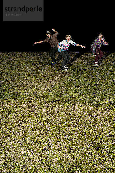 Freunde skateboarden nachts auf Grasfeld