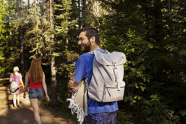 Lächelnder Mann mit Rucksack  der mit Mutter und Schwester an Bäumen im Wald spazieren geht