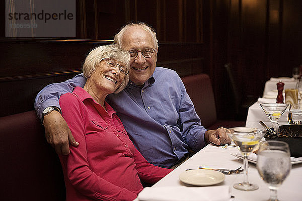 Porträt eines älteren Ehepaares mit Arm um den Arm im Restaurant sitzend