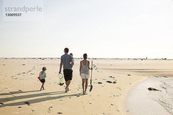 Rückansicht einer Familie  die bei klarem Himmel am Strand spazieren geht