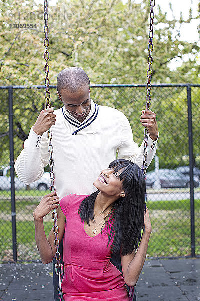 Lächelndes Paar schaut sich an  während es im Park mit der Schaukel spielt