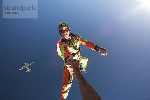 Mann hält Freunden die Hand  während BASE in den Himmel springt