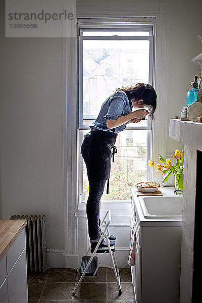 Seitenansicht einer Frau  die Kuchen fotografiert  während sie auf einer Stufenleiter steht