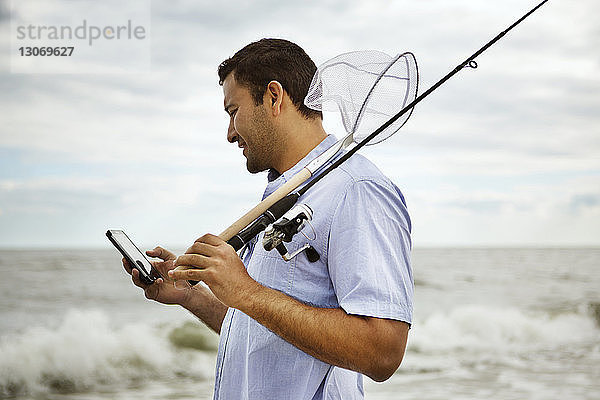Mann hält Angelrute mit Mobiltelefon  während er auf See steht