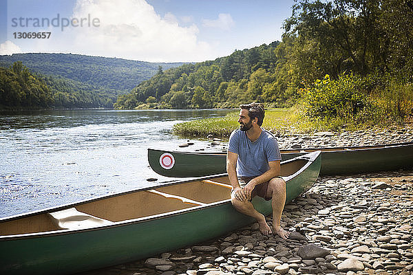 Mann schaut weg  während er auf einem Kanu am Seeufer sitzt