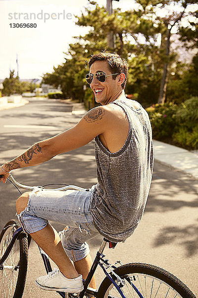 Seitenansicht eines glücklichen Mannes beim Fahrradfahren auf der Straße