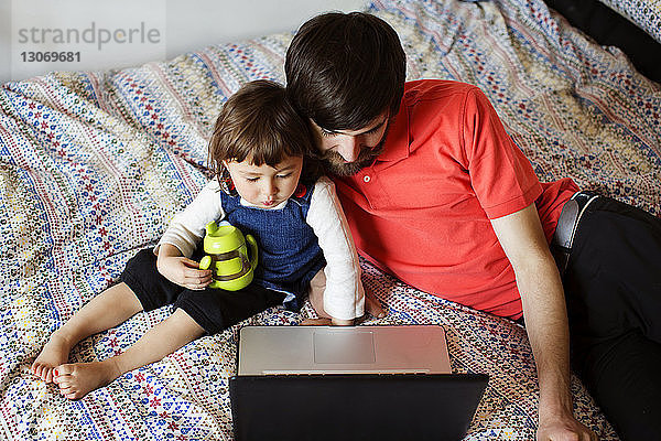 Hochwinkelansicht von Vater und Tochter  die auf einen Laptop-Computer schauen  während sie sich im Bett entspannen