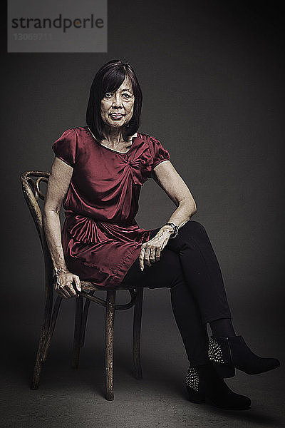 Porträt einer älteren Frau  die auf einem Stuhl vor schwarzem Hintergrund sitzt