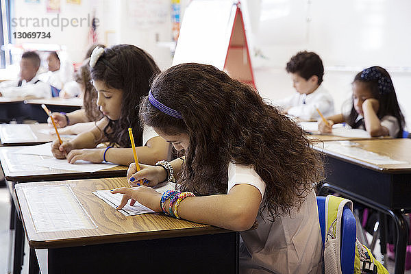 Schülerinnen und Schüler schreiben im Klassenzimmer auf Arbeitsblättern