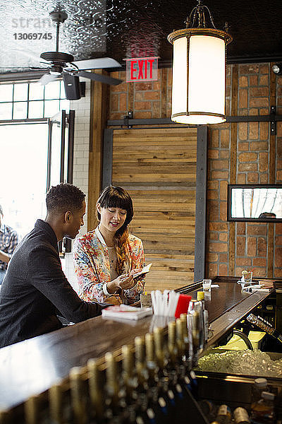Frau zeigt einem Freund ein kleines Buch  während sie in einer Bar sitzt