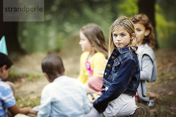 Porträt eines Mädchens  das mit Freunden auf einem Feld im Park sitzt