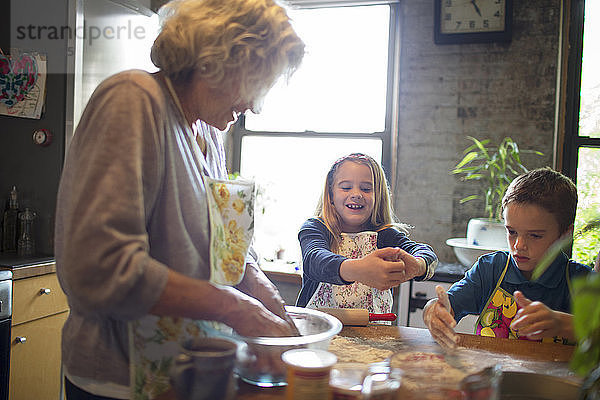 Glückliche Kinder mit Großmutter beim Mehlmischen in der Küche
