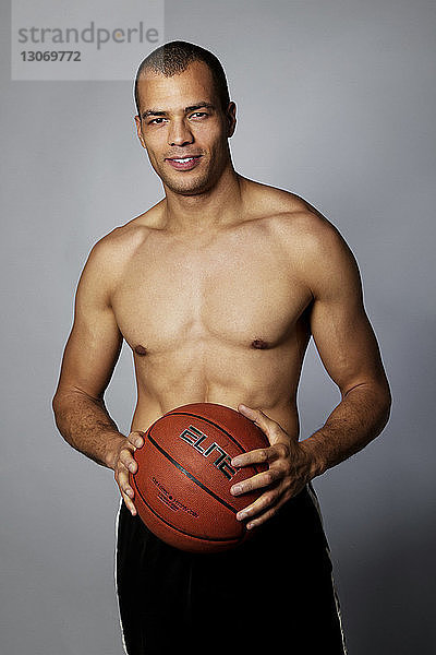 Porträt eines Mannes  der einen Basketball hält  während er vor grauem Hintergrund steht
