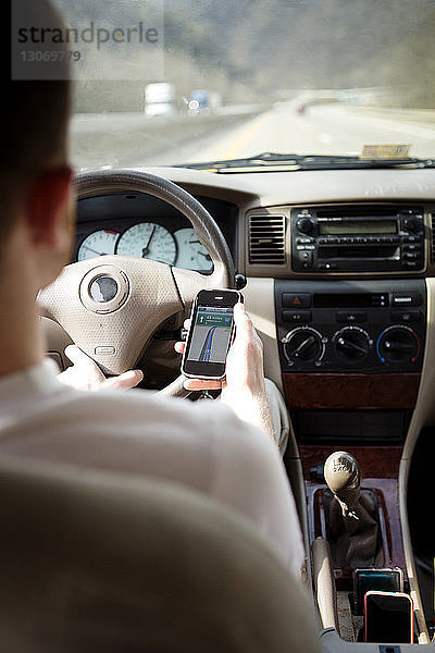 Rückansicht eines Mannes  der während der Fahrt im Auto ein Smartphone benutzt