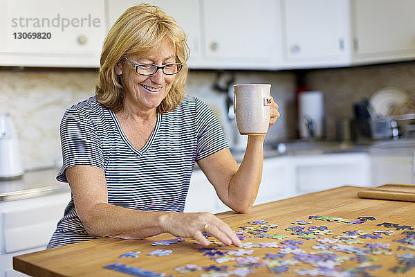 Glückliche Frau hält Becher  während sie zu Hause Puzzle spielt