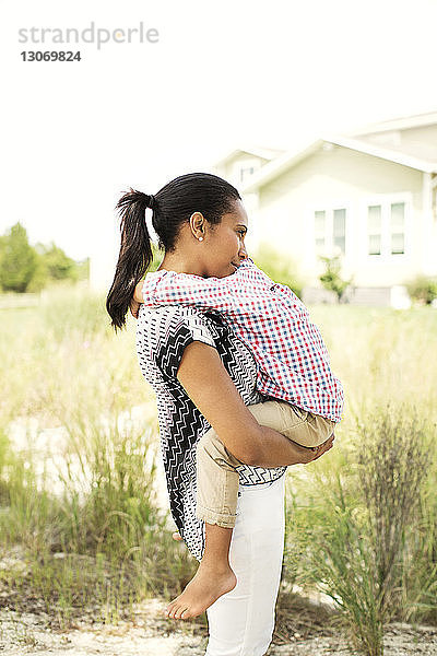 Glückliche Frau umarmt Sohn  während sie im Hinterhof vor klarem Himmel steht