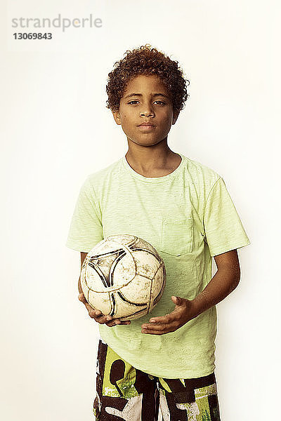 Porträt eines Jungen mit Fussball in der Hand vor klarem Himmel