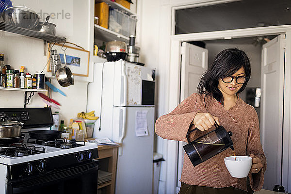 Frau gießt Kaffee in Tasse ein  während sie in der Küche steht