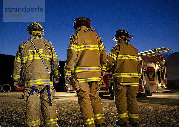 Rückansicht von Feuerwehrleuten  die nachts gegen den Himmel stehen