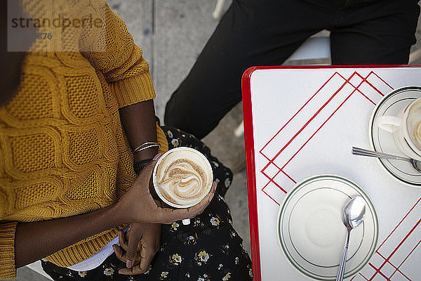 Draufsicht einer Frau mit Cappuccino in der Hand  während sie im Straßencafé sitzt