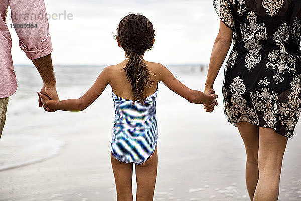 Mitschnitt der Eltern  die die Hände der Tochter beim Strandspaziergang halten