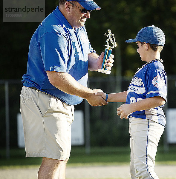 Trainer übergibt Trophäe an Jungen auf Baseballfeld