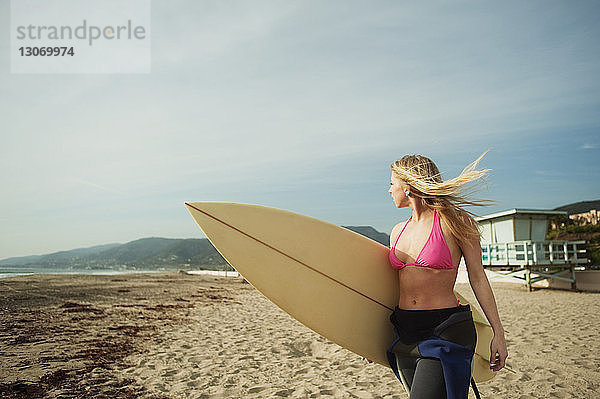 Frau mit Surfbrett  die beim Strandspaziergang am Ufer wegschaut