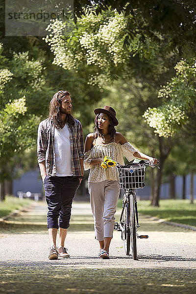 Paar in voller Länge zu Fuß mit dem Fahrrad auf dem Fußweg im Park