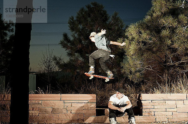 Mann mit Skateboard springt über Freund
