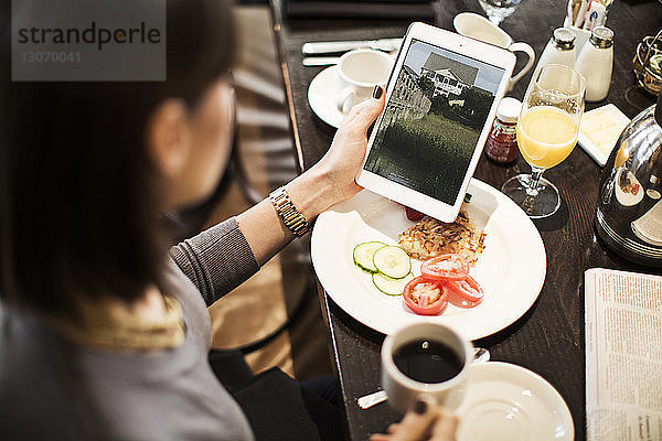 Hochwinkelansicht einer Frau  die einen Tablet-Computer benutzt  während sie im Restaurant am Tisch sitzt