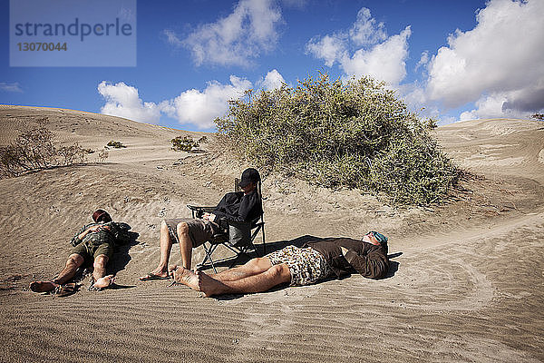 Freunde entspannen sich bei Sonnenschein am Sandstrand gegen den Himmel