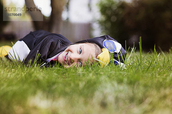 Porträt eines lächelnden Mädchens in Halloween-Kostüm auf dem Rasen liegend