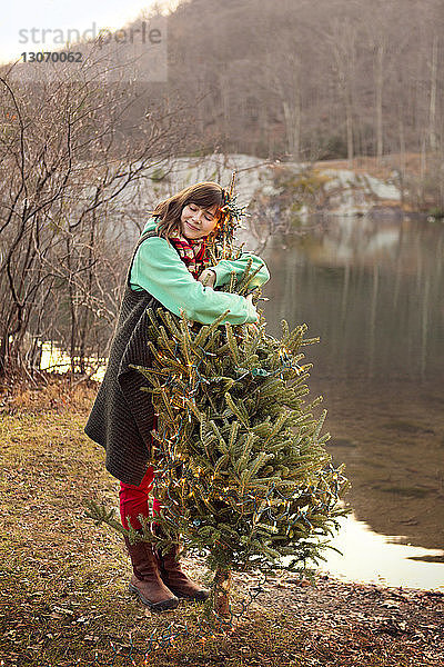 Frau umarmt Weihnachtsbaum am Seeufer