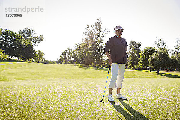 Glückliche Frau schaut weg  während sie am Golfplatz vor klarem Himmel steht