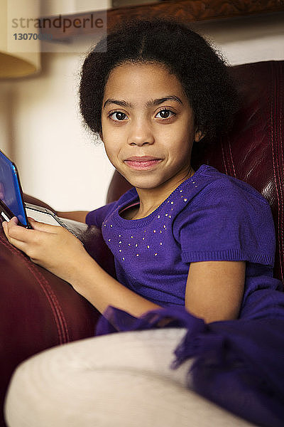 Porträt eines Mädchens  das ein Videospiel in der Hand hält  während es zu Hause auf dem Sofa sitzt