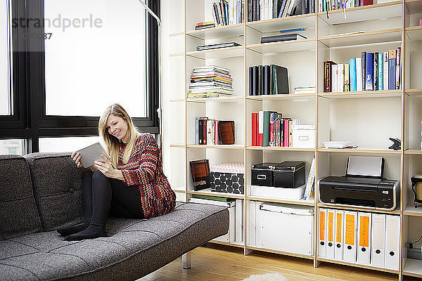 Frau benutzt Tablet-Computer  während sie zu Hause auf dem Sofa sitzt