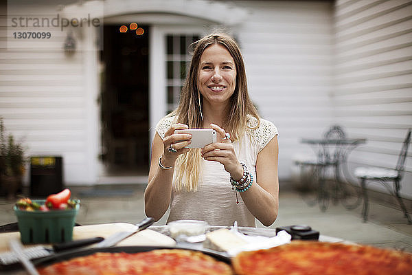 Porträt einer Frau  die ein Smartphone in der Hand hält  während sie auf dem Rasen am Tisch sitzt