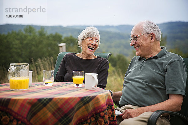Glückliches älteres Ehepaar sitzt am Tisch auf dem Rasen